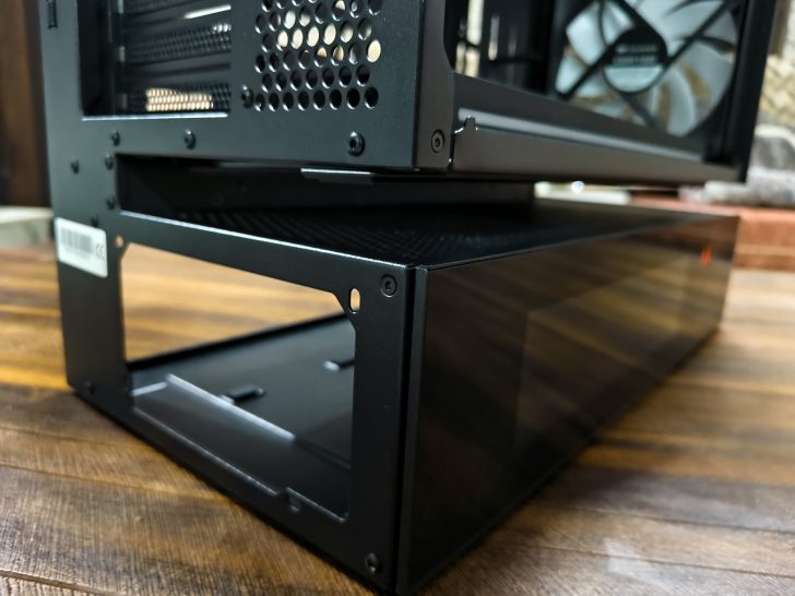 A close-up of a black PC case featuring a mesh panel and a glass side, sitting on a wooden surface.