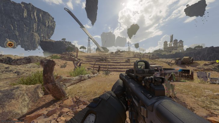 A first-person shooter view in a game set in a desert landscape with floating rocks, a large sword, and an on-screen objective icon on the left.