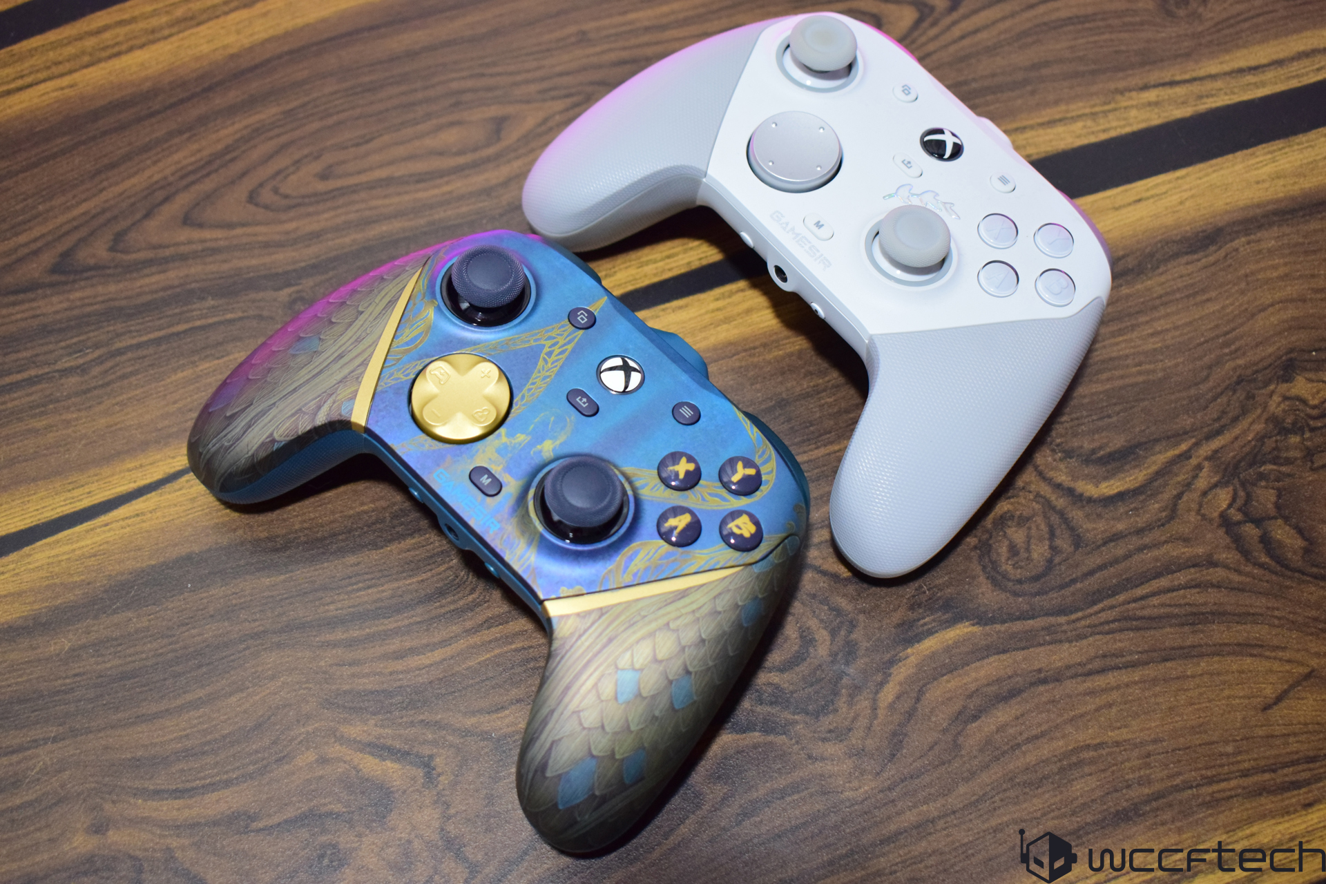 Two Xbox wireless controllers on a wooden table, one with a blue and gold design and the other in white with GAMER text.