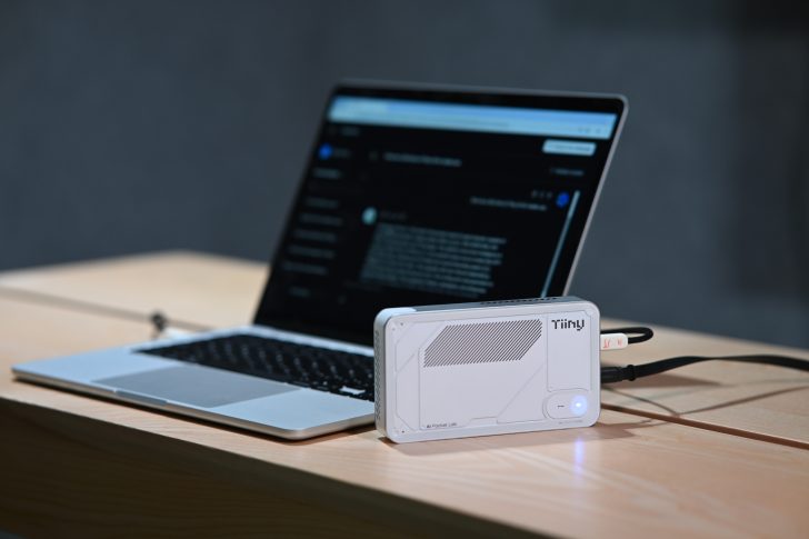 A Tiiny AI Pocket Lab device is connected to a laptop displaying an application with text on its screen.
