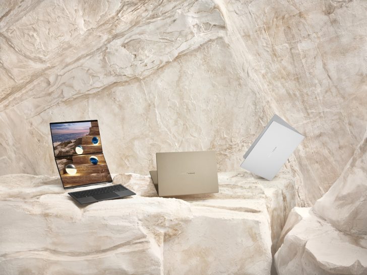 Three OpenBook devices are displayed on a rock surface, showcasing their flexible dual-display and compact design, with one open showing a desert landscape image across both screens.